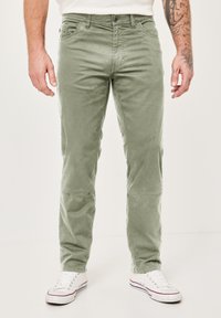 Hellgrüne Cordhose mit geradem Schnitt, fünf Taschen und Knopfverschluss, kombiniert mit weißen Sneakers.