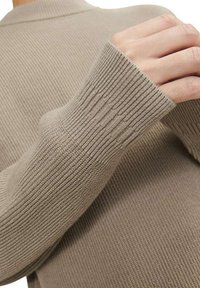 Pull en maille à manches longues couleur beige clair, avec une texture côtelée, un col monté et des poignets ajustés. Matière douce avec un léger lustre.