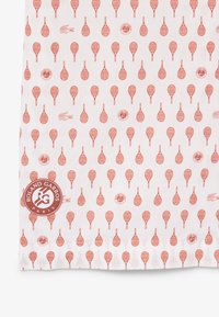 Tessuto bianco con un motivo ripetuto di racchette da tennis rosse, loghi Roland Garros e piccoli loghi del coccodrillo Lacoste.