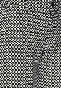 Svart och vit mönstrad tyg med ett zigzag-mönster, synlig sömnad och en svart knapp vid midjan.