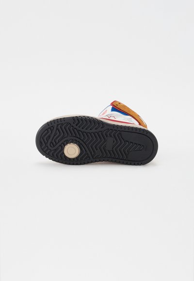 Zapatilla multicolor con una parte superior texturizada blanca, acentos marrones y una suela de goma negra con patrones en zigzag y detalles circulares.