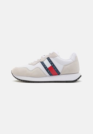 Zapatillas hechas de cuero blanco y ante gris claro con una suela de goma negra. Presenta rayas horizontales rojas y marinas y la marca "TOMMY JEANS".