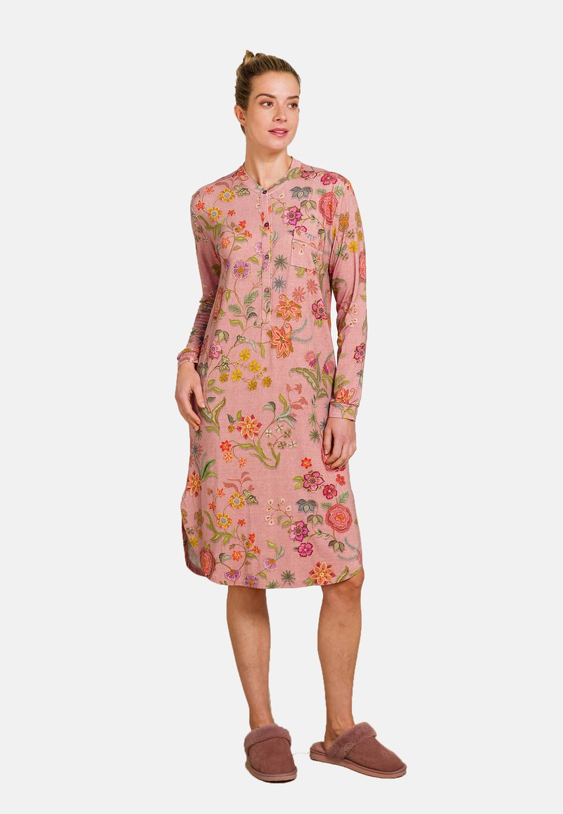 Langloof roze jurk met bloemborduursel, voorzien van een knoopsluiting bij de hals en zijsplitten, gecombineerd met bruine fuzzy slippers.