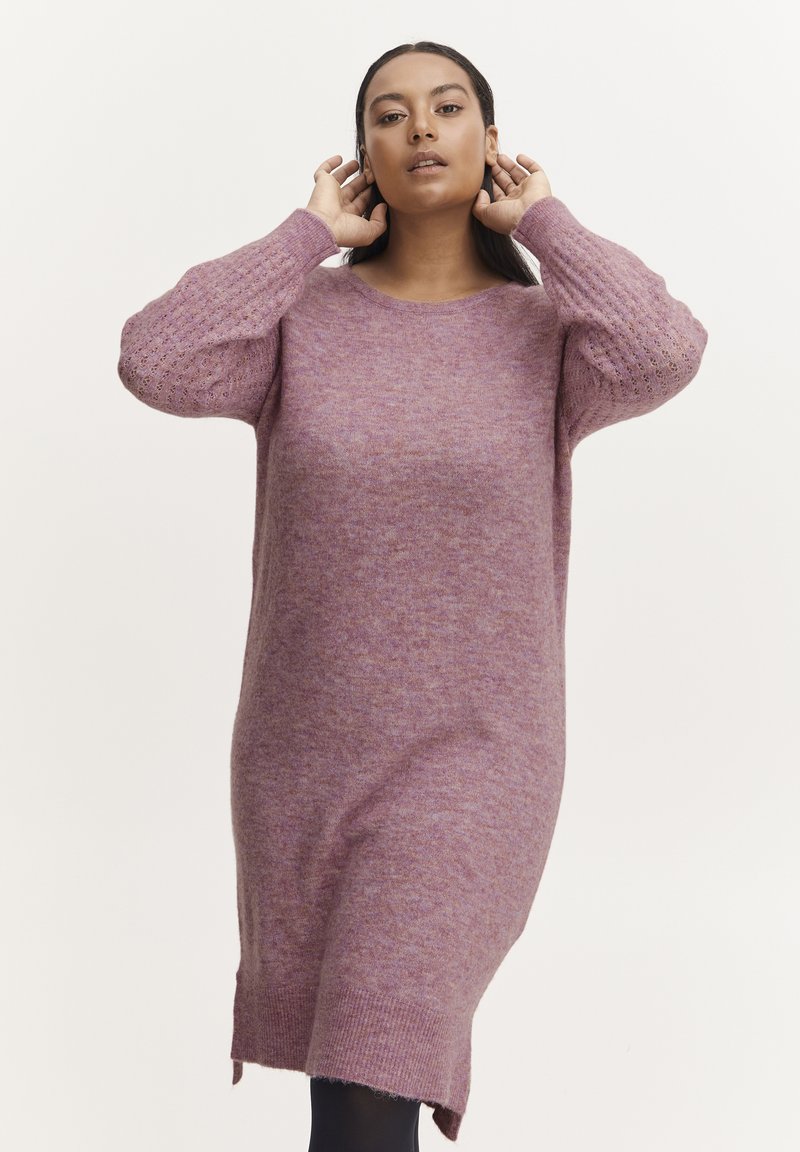 Abito maglione viola in maglia con maniche lunghe, scollatura rotonda e motivi a rilievo sulle maniche. Presenta spacco laterale per una maggiore libertà di movimento.