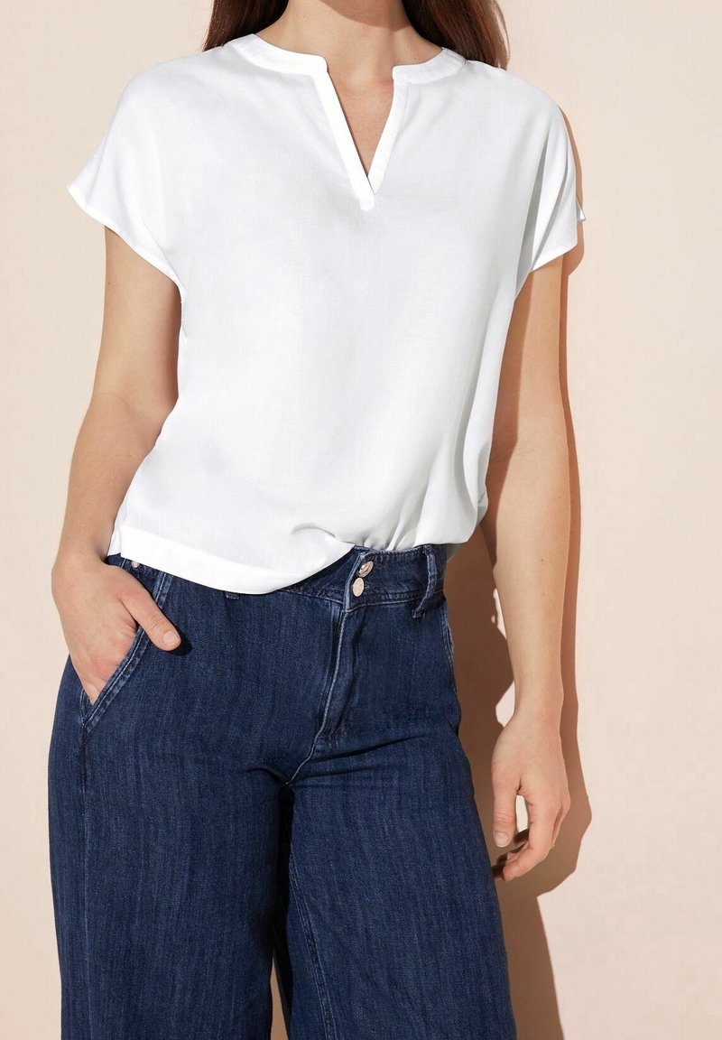 Top bianco a maniche corte con scollo aV, abbinato a jeans in denim scuro a vita alta. Tessuto morbido e vestibilità comoda.