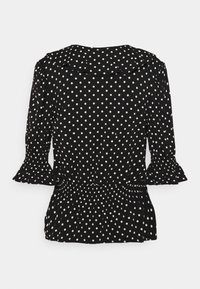 Svart blus med vita prickar, volangkrage och -ärmar, elastisk midja och ärmar i trekvarts längd.