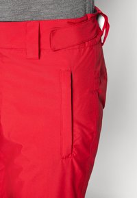Pantalons rouges en tissu lisse avec une poche latérale et une passante de ceinture. La taille est dotée d'un système de fermeture à crochet et boucle pour un ajustement.