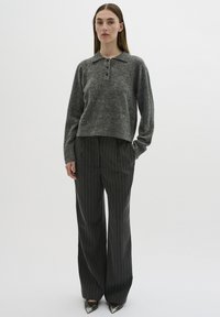 Gray wool sweater with a collar, three buttons, and ribbed hem, paired with dark pinstriped trousers and pointed metallic shoes.