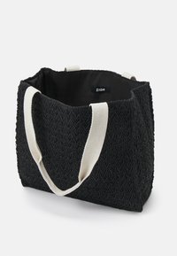 Černá pletená taška přes rameno s bílými tkaninovými uchy a malou vnitřní štítkou s nápisem "ZIGN," otevřená z vrchu na bílém pozadí.