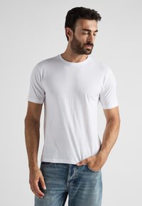 Vit kortärmad t-shirt i ett mjukt tyg med rund halsringning, bärs tillsammans med blå denim jeans. Enkelt design, inga synliga mönster eller logotyper.