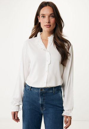 Blusa blanca con cuello fruncido y cierre de botones, mangas largas con puños gathered, combinada con unos vaqueros de tiro alto azules.