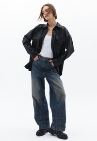 Zwarte faux-lederen shirtjack met twee voorkruiden, gecombineerd met losse vervaagde blauwe denim jeans en zwarte platform schoenen.