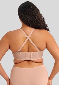 Sostén beige con tirantes cruzados, textura de tela y cierre de gancho en la parte posterior. Combinado con ropa interior beige.