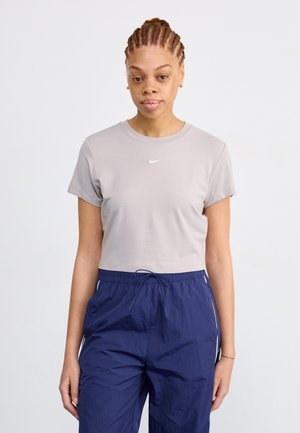 Lichtgrijs cropped t-shirt met korte mouwen, voorzien van een klein wit Nike-logo, gecombineerd met marineblauwe broek met trekkoord en een gestructureerde afwerking.