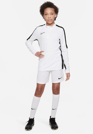 Weißes Nike Langarmshirt mit schwarzen Akzenten, kombiniert mit weißen Shorts und knielangen weißen Socken. Schwarze Fußballschuhe runden das Outfit ab.