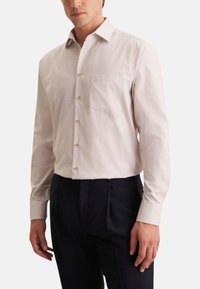 Camicia chiara a maniche lunghe con un piccolo motivo a pois, con colletto e taschino sul petto, abbinata a pantaloni scuri.