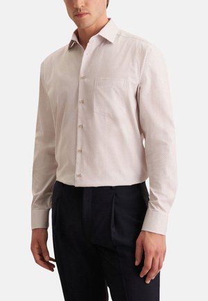 Camicia chiara a maniche lunghe con un piccolo motivo a pois, con colletto e taschino sul petto, abbinata a pantaloni scuri.