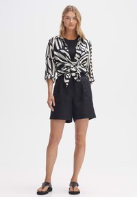 Maglietta a righe bianco e nero con maniche corte, annodata in vita, abbinata a pantaloni corti neri e sandali neri. Tessuto liscio, vestibilità casual.