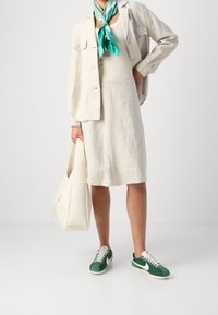 Giacca e gonna di lino in un beige chiaro, abbinate a delle sneaker verdi e bianche. Accessoriate con una sciarpa di seta color turchese e una borsa bianca.