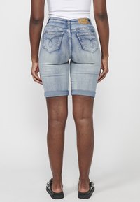 Shorts en denim délavé bleu clair avec ourlets roulés. Dotés de poches arrières avec des détails de couture et d'un patch en cuir de marque sur la taille.