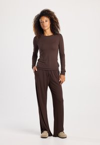Brown long-sleeve top paired with matching loose-fitting pants, both made of soft fabric. The outfit features a drawstring waist and relaxed fit.