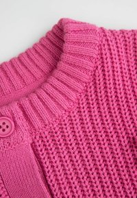 Różowy sweterek wykonany na drutach z żeberkowym kołnierzem, teksturowanym wzorem i okrągłym zapięciem na guzik. Miękka tkanina o jednolitym kolorze.