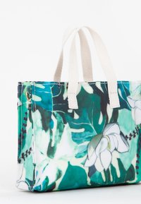Tote taske med hvide stoffer håndtag og et grønt, teal og hvidt blomstermønster samt bladdesign på stofkroppen.