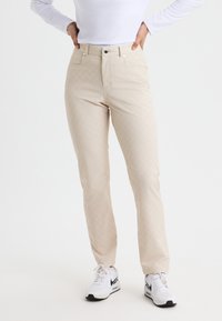 Beige mönstrade byxor med en diamantdesign, två framfickor och en klassisk passform, i kombination med vita sneakers.