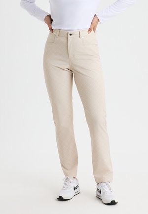Beige gemusterte Hose mit Rautendesign, zwei Vordertaschen und klassischer Passform, kombiniert mit weißen Sneakern.