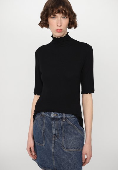 Top preto, justo, com gola alta e mangas curtas e bufantes; combinado com uma saia de ganga azul com bolsos frontais e fecho de botão.