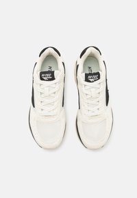 White sneakers with black accents and textured mesh upper. Features a padded collar, flat laces, and a rubber sole. Brand logo on the tongue.