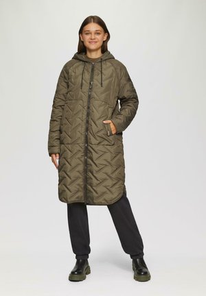 Long olive green quilted coat with a hood, zip closure, and side pockets. The jacket features a textured pattern and is paired with black pants and boots.