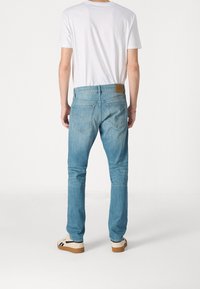 Ljusblå denimjeans med rak bendesign, med bakfickor och en brun läderlogotyp på midjan. Enkel vit t-shirt.