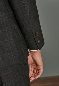 Blazer à carreaux foncé sur mesure avec tissu texturé. Comprend des boutons marron et une ouverture de manchette, mettant en valeur des éléments de design professionnels.