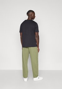 Μαύρο μπλουζάκι με κοντό μανίκι, συνδυασμένο με χαλαρά, χακί παντελόνια και λευκά αθλητικά παπούτσια, σε προβολή από πίσω. Λείο ύφασμα, άνετη γραμμή.