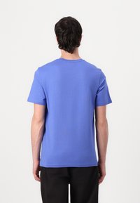 T-shirt en coton bleu vu de dos, avec des manches courtes, un col rond et une texture lisse et uniforme. Aucun logo ou motif visible.