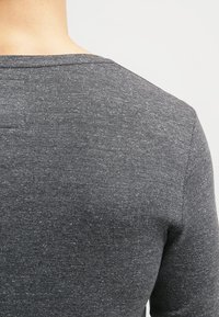 Grå långärmad skjorta gjord av mjukt tyg med rund halsringning, med en texturerad yta och svaga prickiga detaljer.