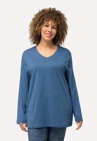 Blaues Langarmshirt mit V-Ausschnitt, aus weichem Stoff, mit einer lockeren Passform. Kombiniert mit blauen Jeanshosen.