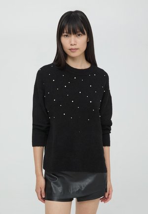 Maglione nero lavorato a maglia con decorazioni in perle, scollatura rotonda, maniche ¾ e vestibilità svasata, abbinato a una mini gonna in pelle nera.