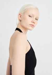 Black halter-neck dress with a low back design; smooth texture and fitted silhouette. Model has short blonde hair and minimal accessories.