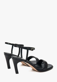 Zwarte leren hoge hakken sandalen met twee brede voorkleppen, een enkelbandje en een gouden gesp accent op een taps toelopende hak. Gladde oppervlakte.