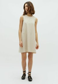 Beiges ärmelloses Kleid, knielang, mit einfachem Design und subtiler Textur. Kombiniert mit schwarzen Ankle-strap-Schuhen.
