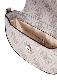 Bolso Guess beige y topo con patrón, con solapa abierta que muestra el forro interior beige estampado con logotipos de Guess y un cierre magnético dorado.