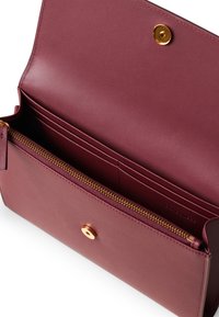 Portafoglio in pelle borgogna con compartimento con zip, slot per carte e chiusura a pressione dorata. Texture liscia con design minimalista.