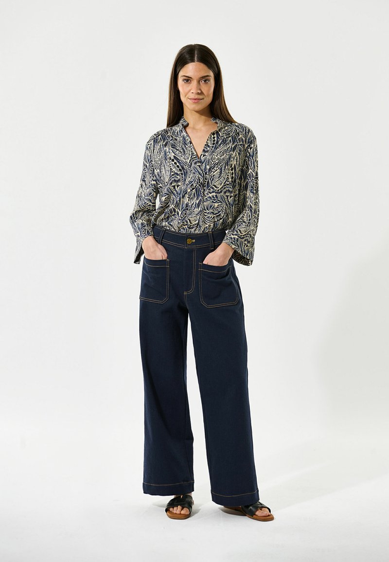 Blusa con estampado floral en azul marino y crema, de mangas largas y con cuello; pantalones anchos de mezclilla oscura de corte holgado con costuras prominentes y bolsillos.