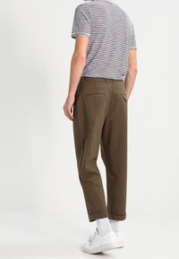 Bruna bomullsbukser med en avslappnad passform, med uppvikta ärmar, två bakfickor, bärs med en randig t-shirt och vita sneakers.