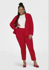 Raudonas kostiumas su pritaikytu švarku ir siaurais džinsais, derinamas su baltu viršumi ir raudonais batais. Ypatingas sklandus audinys ir pritaikytas dizainas.