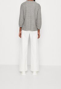 Pullover grigio con maniche a sbuffo a tre quarti, indossato con pantaloni bianchi a gamba larga, mostrato dalla vista posteriore. Tessuto morbido e texturizzato.