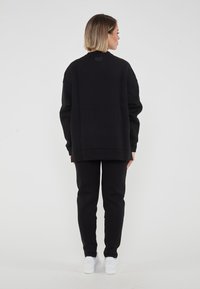 Set di felpa e pantaloni neri in morbido tessuto. La felpa presenta un collo tondo, maniche lunghe e un logo discreto sul retro.