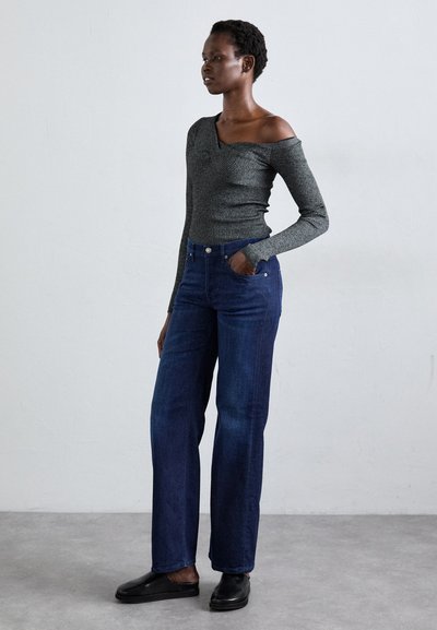 Top gris acanalado de hombros caídos combinado con jeans azules de cintura alta. Los jeans cuentan con bolsillos delanteros y un corte recto, completados con zapatos negros.